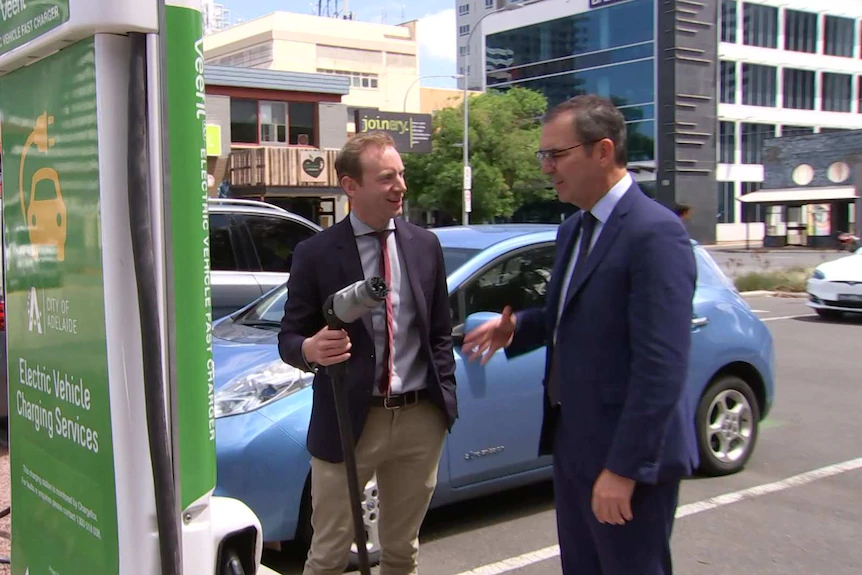 A man holds an electric car plug with another man