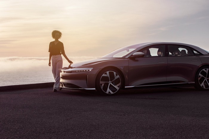 A person standing next to a parked Lucid Air EV sedan. 