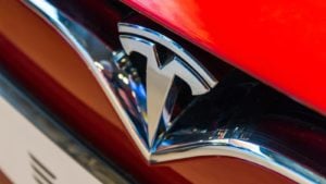A close-up of the Tesla (TSLA) logo on the hood of a red Tesla car.