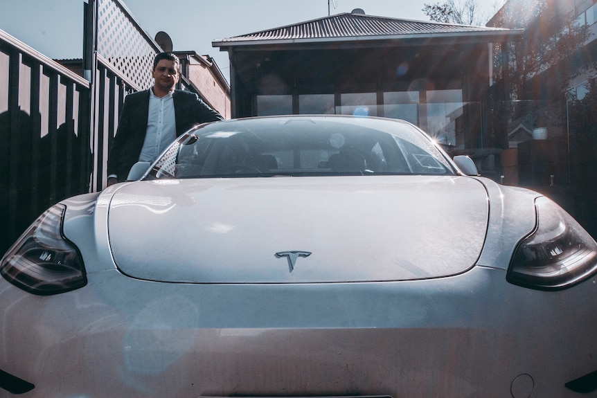 a man in a driveway with an electric car by tesla